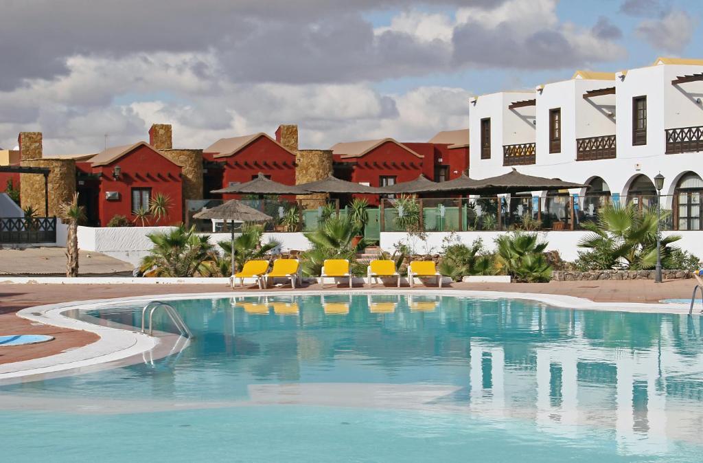 a swimming pool in front of a resort with yellow chairs at Fuerteventura Beach Club in Caleta De Fuste