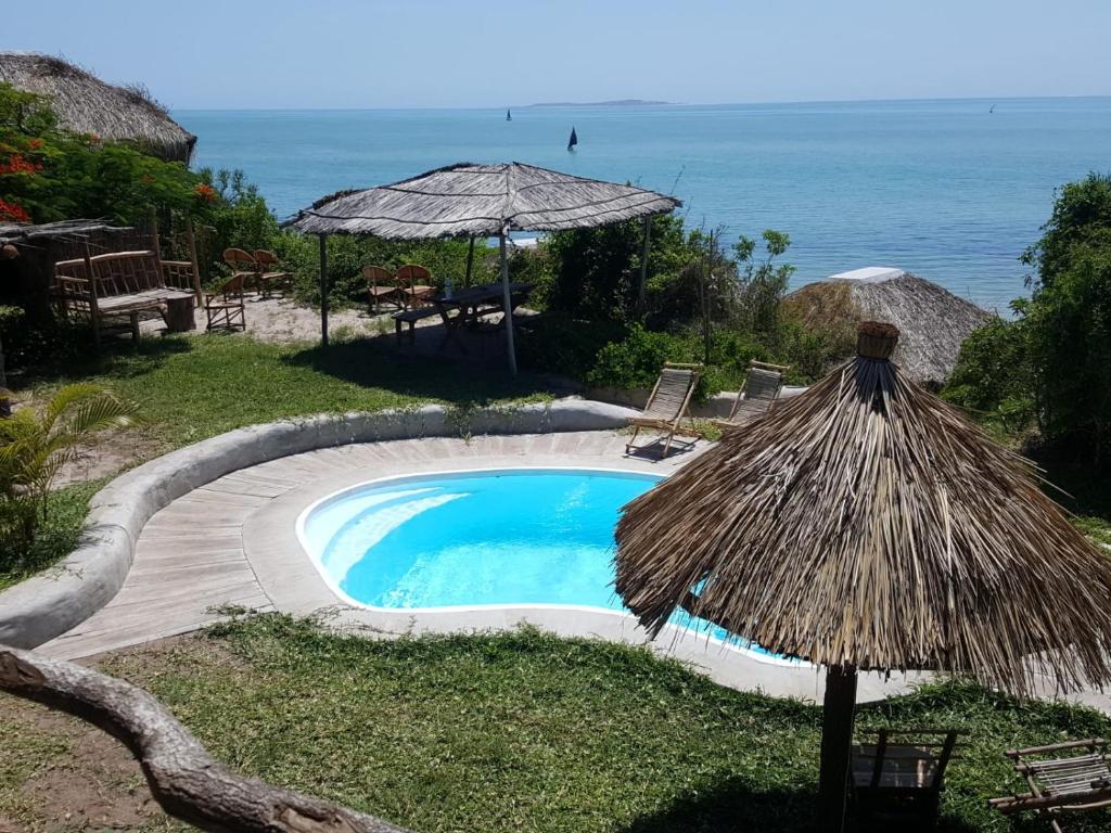 uma pequena piscina com um guarda-sol e o oceano em Baraka Beach Vilanculos em Vilanculos