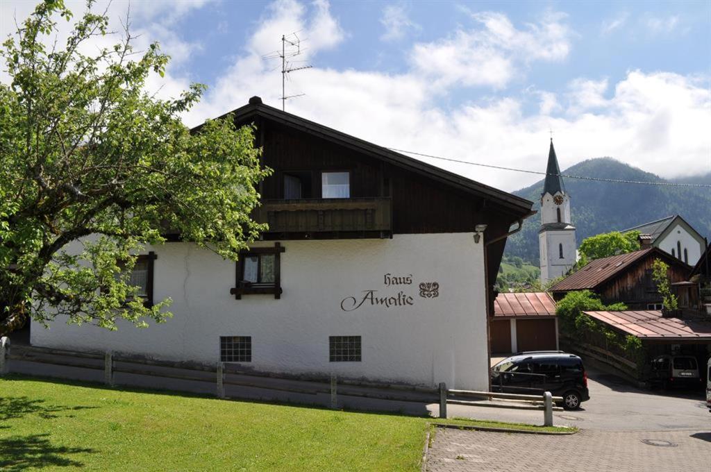 ein weißes Gebäude mit einem Holzdach und einer Kirche in der Unterkunft Haus Amalie in Bad Hindelang