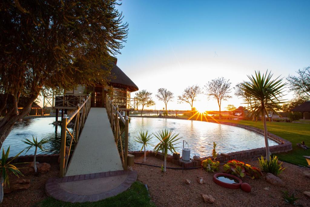a bridge over a pond with a house and trees at Lapa Lange Game Lodge in Mariental