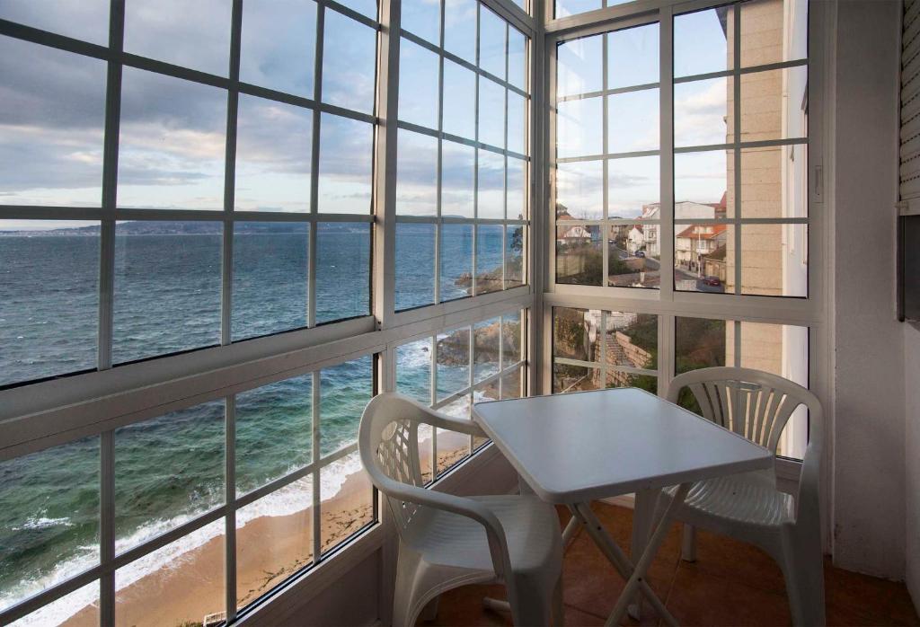 ブエウにあるPRIMERA LÍNEA DE PLAYAの海を望む窓の前にテーブルと椅子