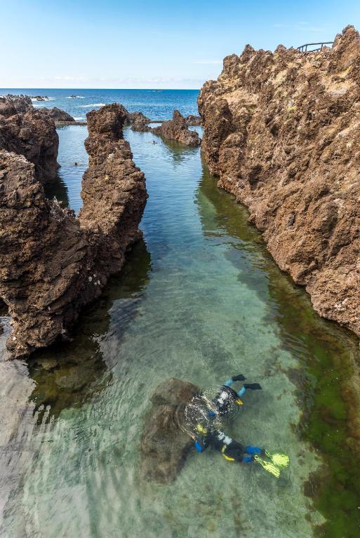a person laying in the water next to some rocks at Aqua Natura Madeira in Porto Moniz
