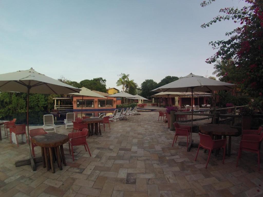an outdoor patio with tables and chairs and umbrellas at Bangalô no alto da colina no Villas do Pratagy - Maceió in Maceió