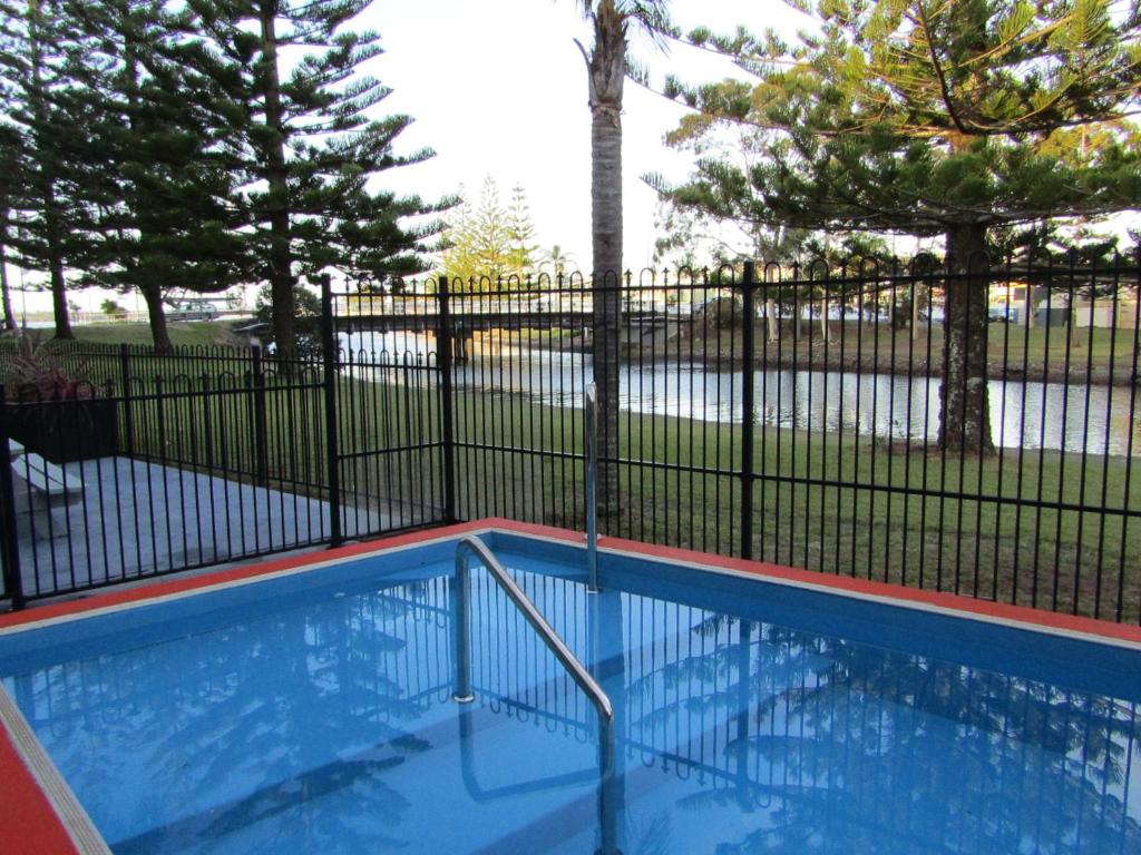 a swimming pool with a metal fence and trees at Le George Motel in Port Macquarie