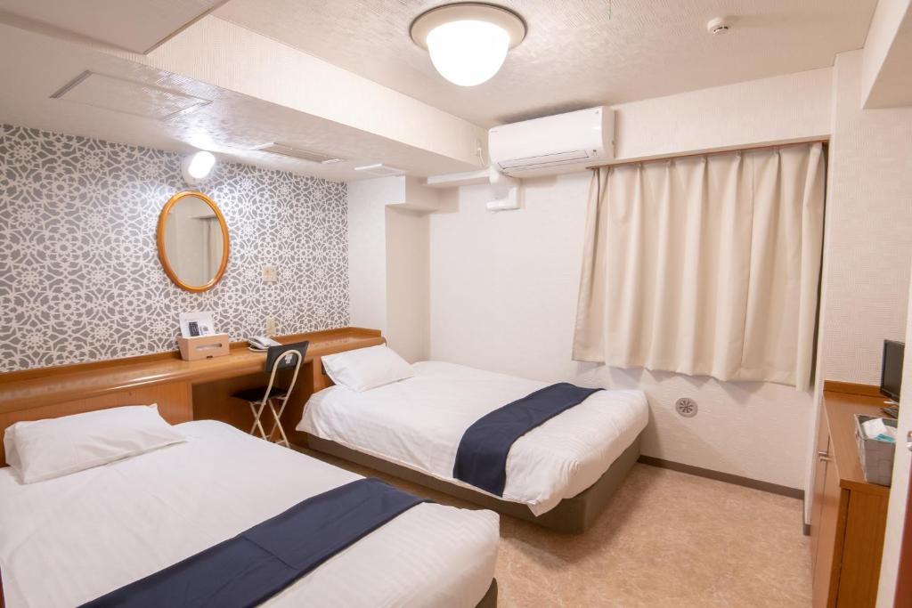 una camera d'albergo con due letti e uno specchio di Kawasaki Station Inn a Kawasaki