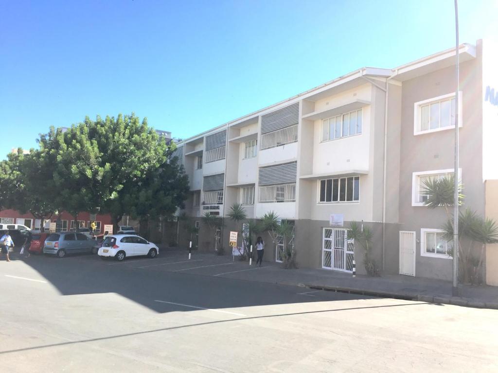 ein Apartmenthaus mit Autos auf einem Parkplatz in der Unterkunft Stern self catering apartments in Windhoek
