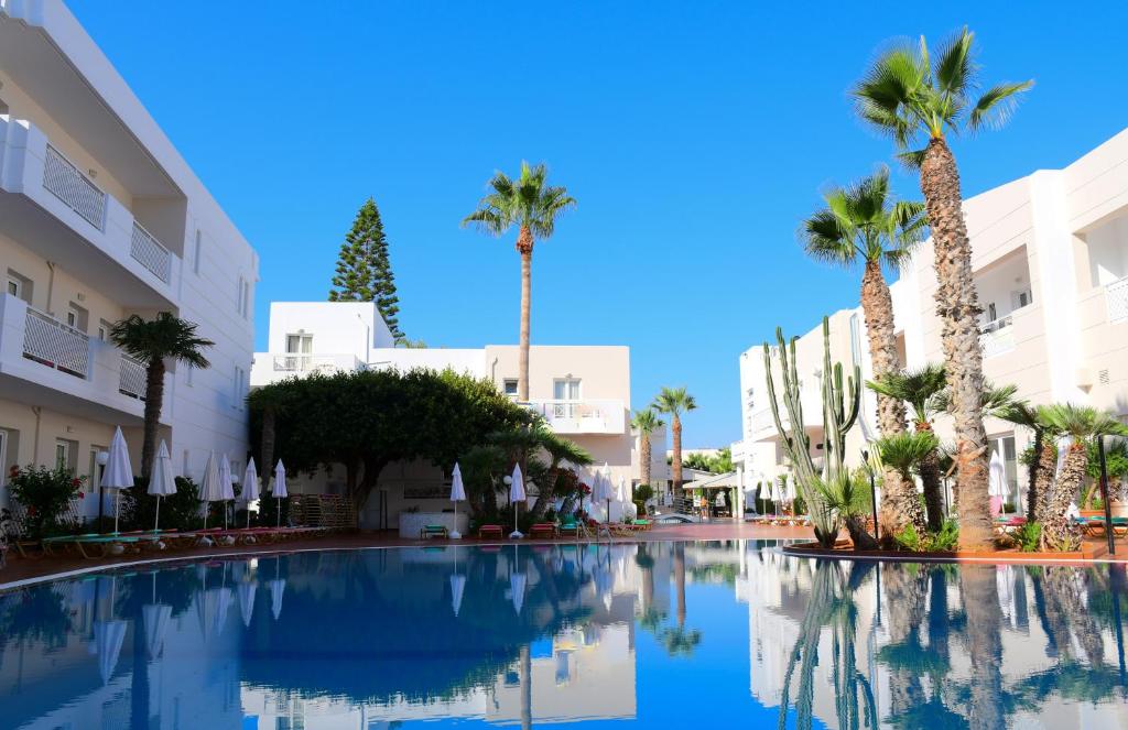 une grande piscine avec des palmiers et des bâtiments dans l'établissement Magda Hotel Club, à Gouves