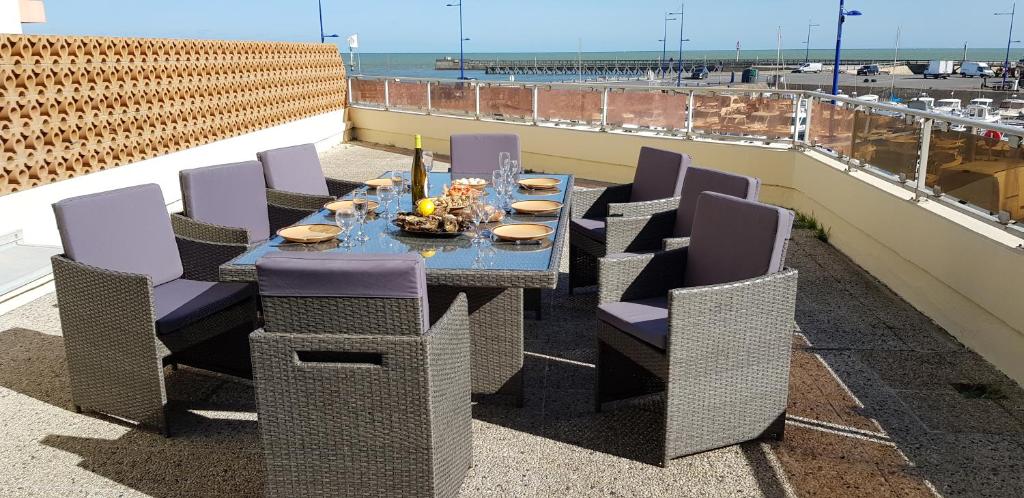 a dining table and chairs on a balcony with the beach at Appartement vue sur mer et port in Grandcamp-Maisy
