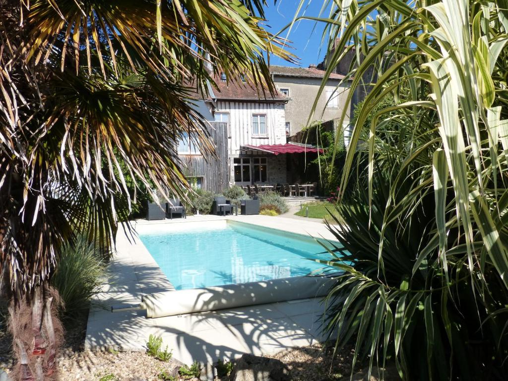 a swimming pool in front of a house with palm trees at Logis Hotel Auberge Dupuytren in Pierre-Buffière