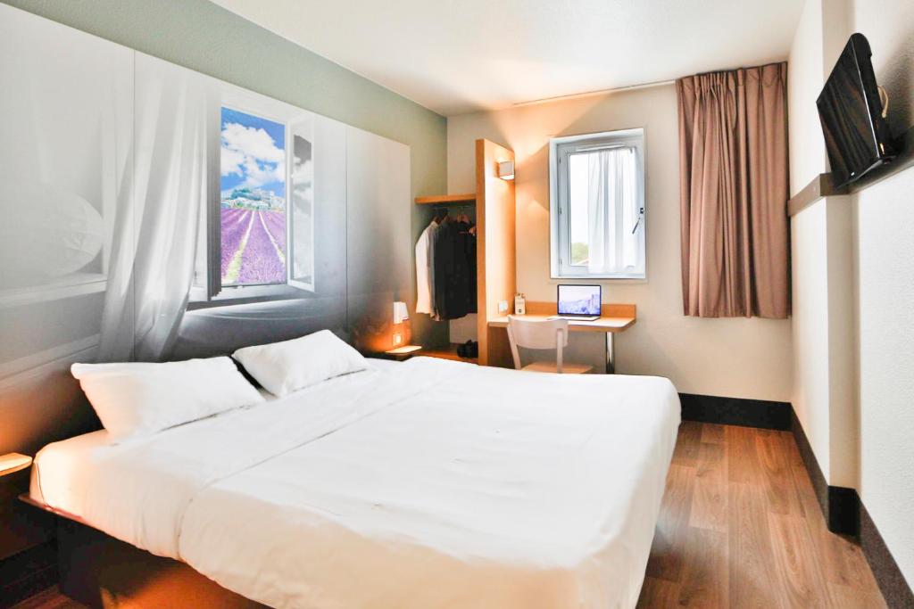 een slaapkamer met een groot wit bed en een bureau bij B&B HOTEL Montélimar Nord in Les Tourrettes