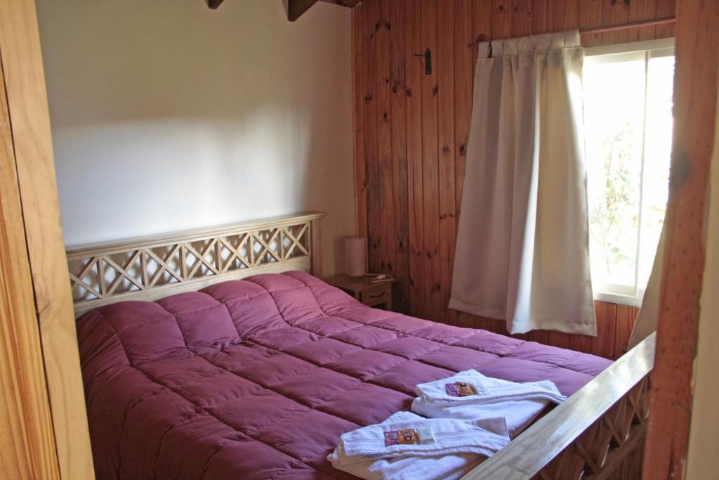 1 cama con sábanas moradas en un dormitorio con ventana en La Casita de Melipal en San Carlos de Bariloche