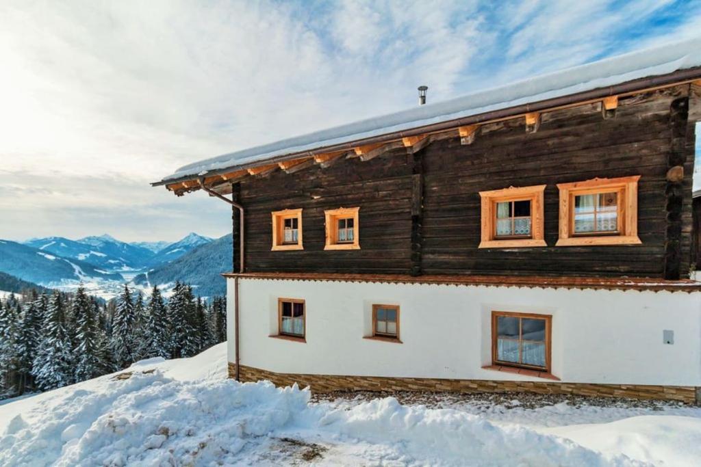 una casa de madera en la nieve con montañas en el fondo en Bauernhütte Niedermaisgut, en Eben im Pongau