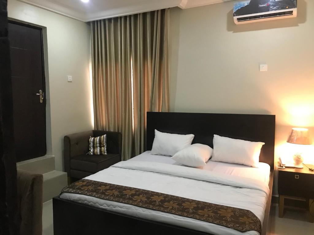 a bedroom with a bed with white sheets and a chair at Choice Suites II in Ikeja