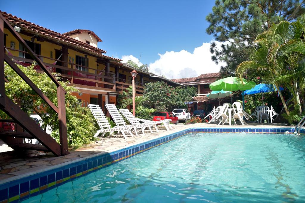 a swimming pool in front of a house with chairs at Pousada Recanto de Minas in Porto Seguro