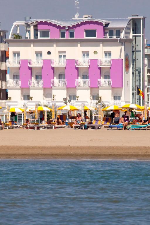 a pink building on the beach with chairs and umbrellas at Hotel Lux in Caorle
