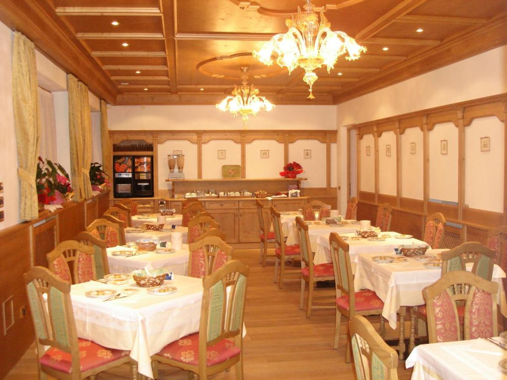 restauracja z białymi stołami i krzesłami oraz żyrandolem w obiekcie Albergo Garnì Ajarnola w mieście Auronzo di Cadore