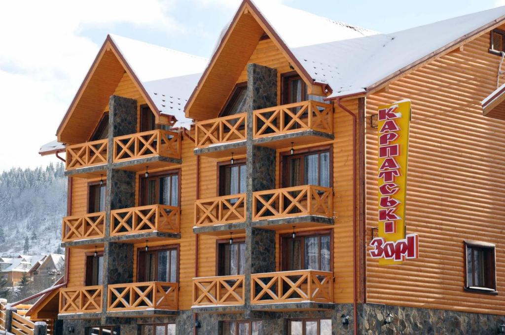 a large wooden building with snow on top of it at Karpatski Zori Hotel in Bukovel