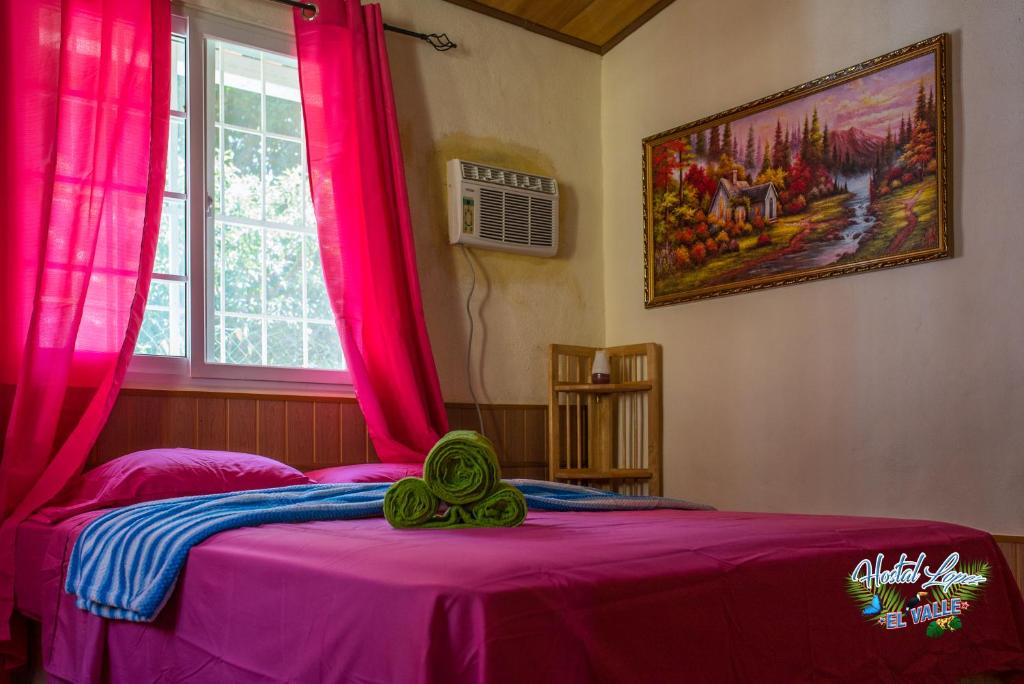 a bed with pink curtains in a room with a window at Hostal Lopez El Valle Cabañas in El Valle