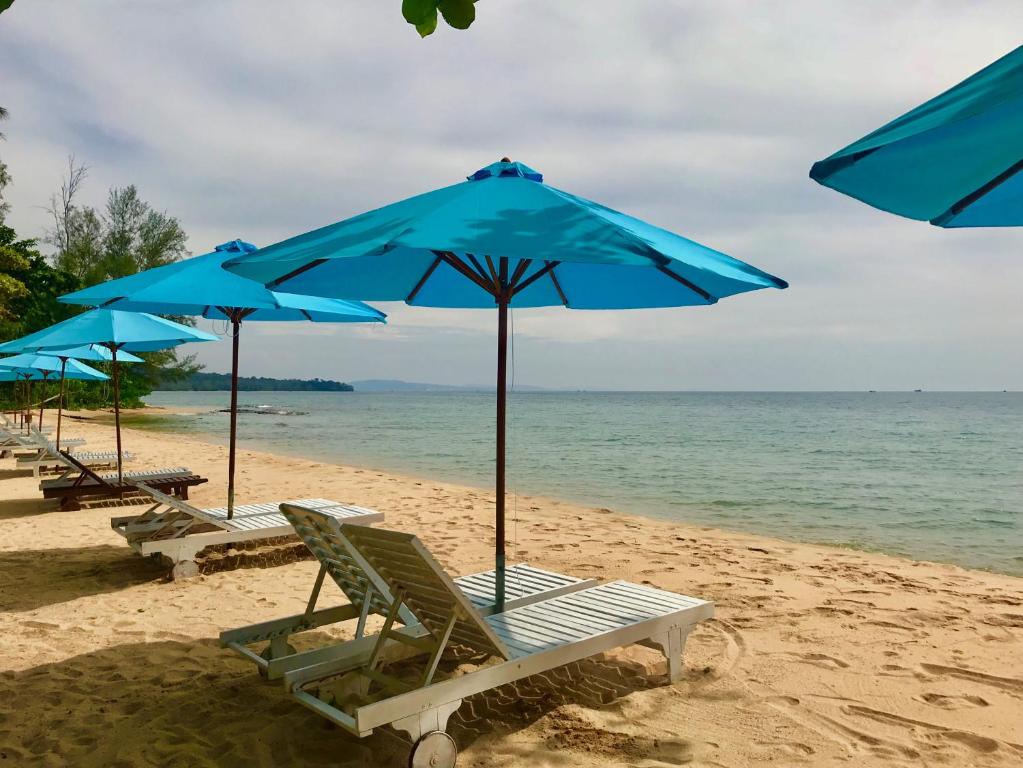 a row of blue beach chairs and umbrellas on a beach at Vung Bau Resort in Phú Quốc
