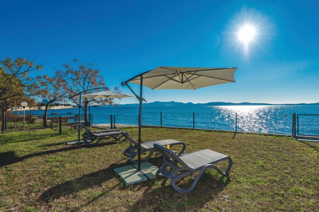 ławka i parasol obok wody w obiekcie Villa Amfora - First row by the sea w Bibinje