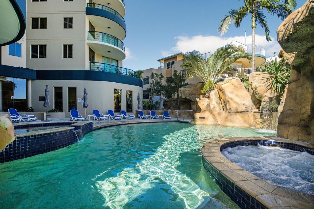 a swimming pool in a resort with chairs and a building at Landmark Resort in Mooloolaba