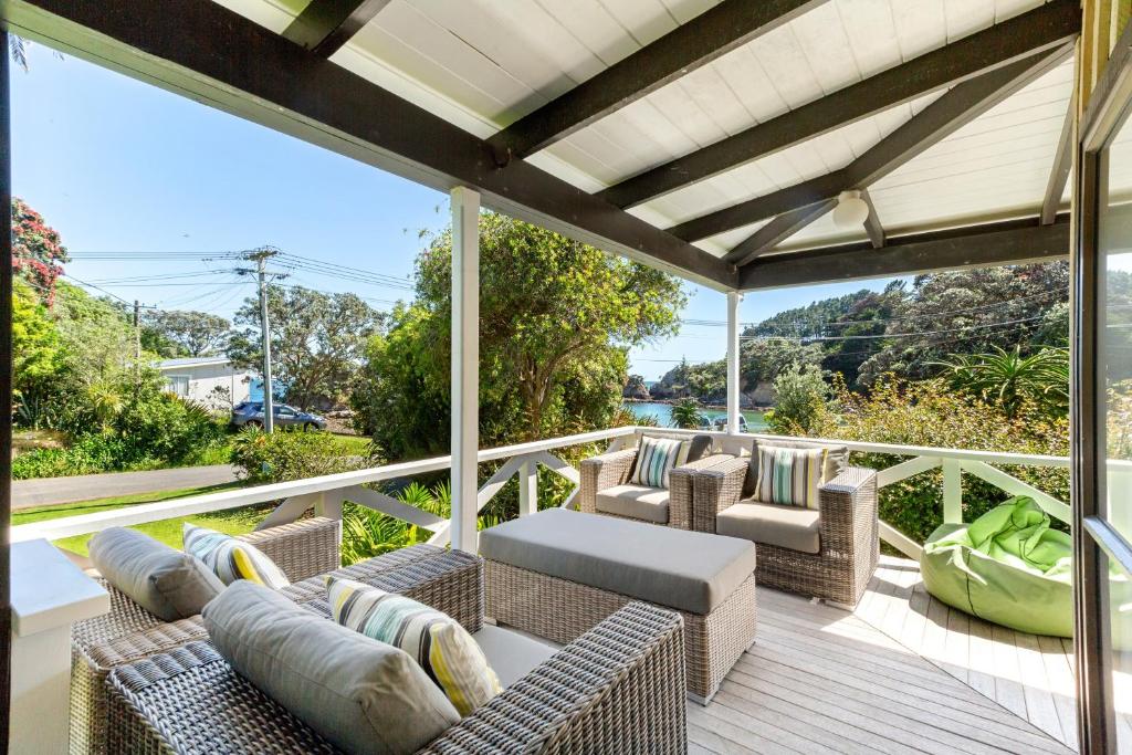 a patio with couches and chairs on a deck at Drop Anchor at Enclosure Bay Beach by Waiheke Unlimited in Oneroa