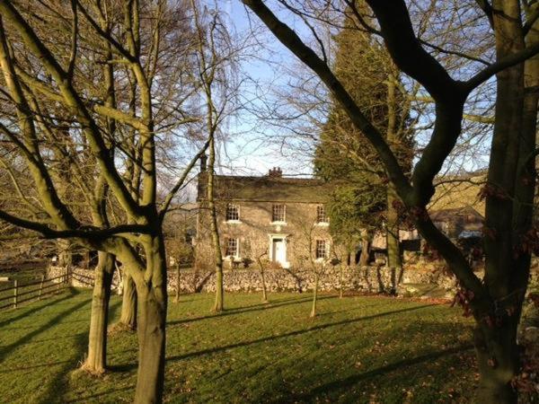 a large stone house with trees in front of it at Bank Top Farm B&B Hartington in Buxton