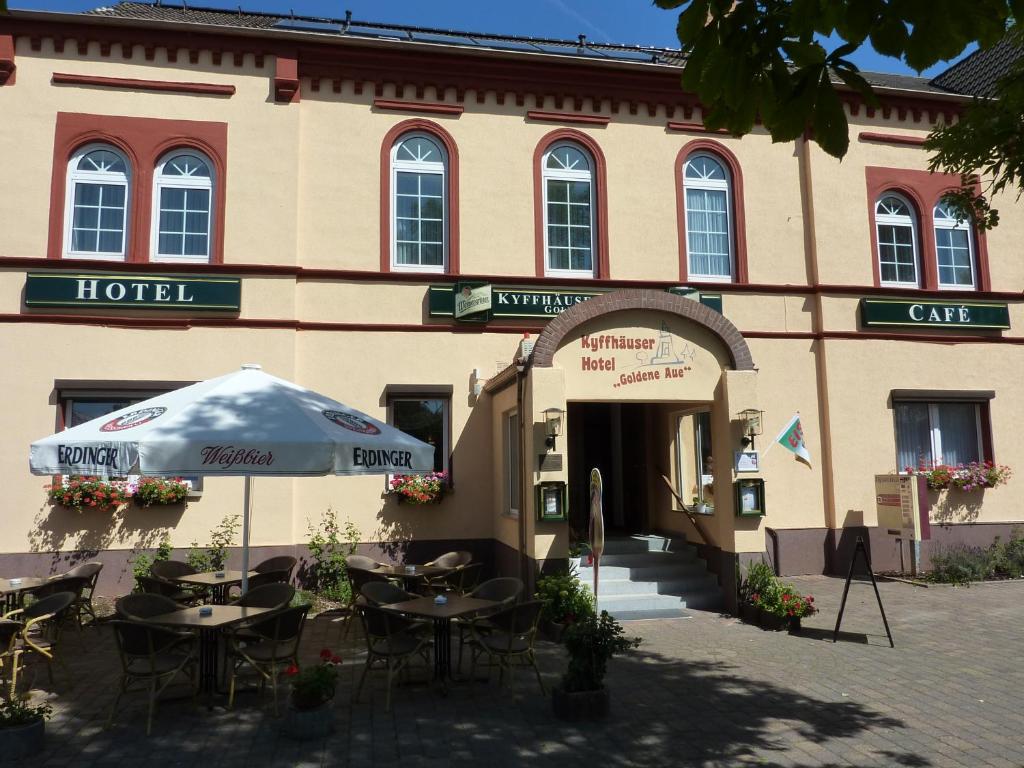 a hotel with tables and an umbrella in front of it at Kyffhäuserhotel "Goldene Aue" in Wallhausen