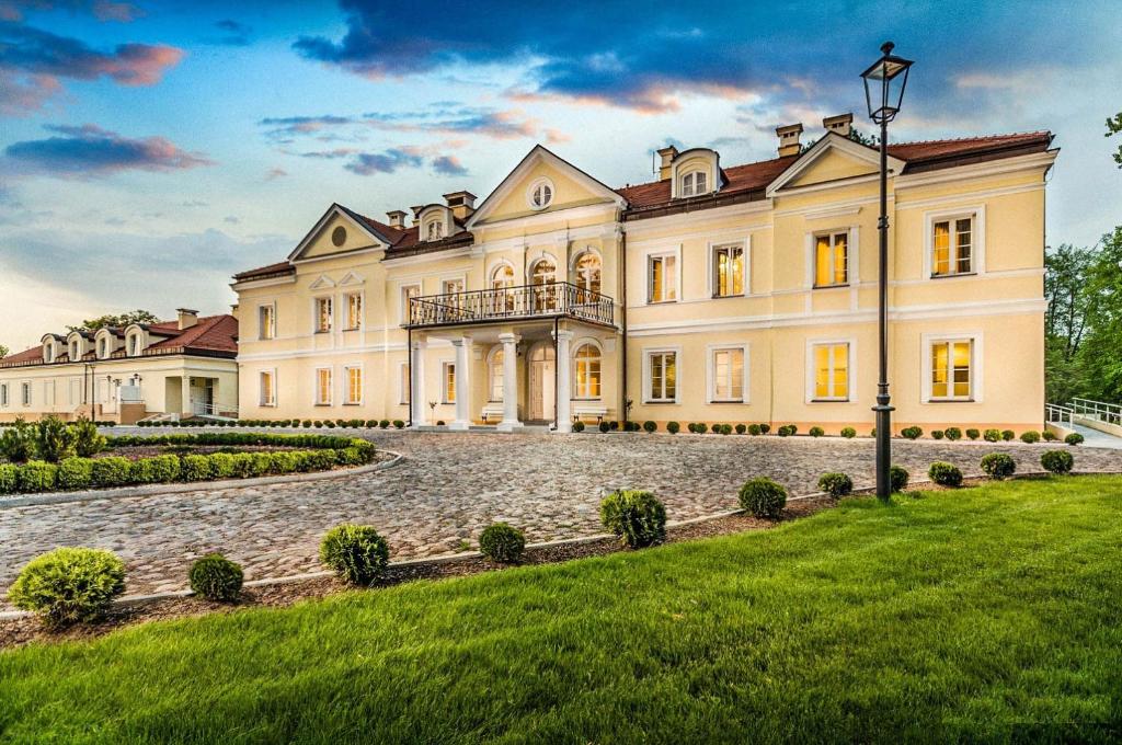a large mansion with a grass yard in front of it at Hotel Sobienie Królewskie in Sobienie Szlacheckie