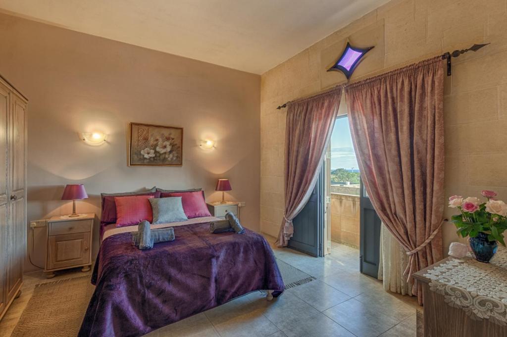 a bedroom with a bed with purple sheets and a window at Ghajn Damma in Xagħra
