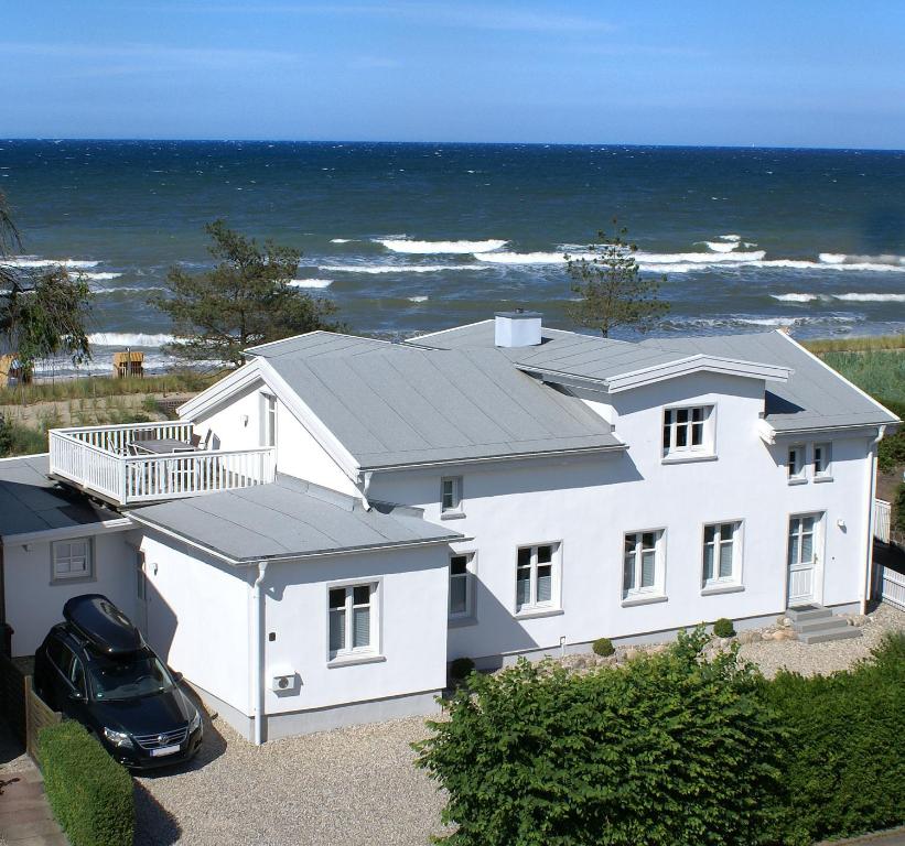 a white house with a car parked in front of the ocean at Meerhaus Niendorf in Niendorf