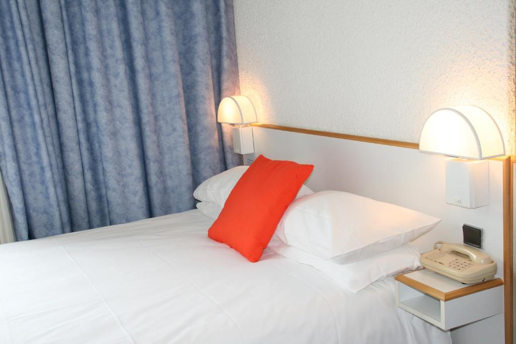 Cama blanca con almohada roja y teléfono en Hôtel des Thermes Les Dômes, en Vichy