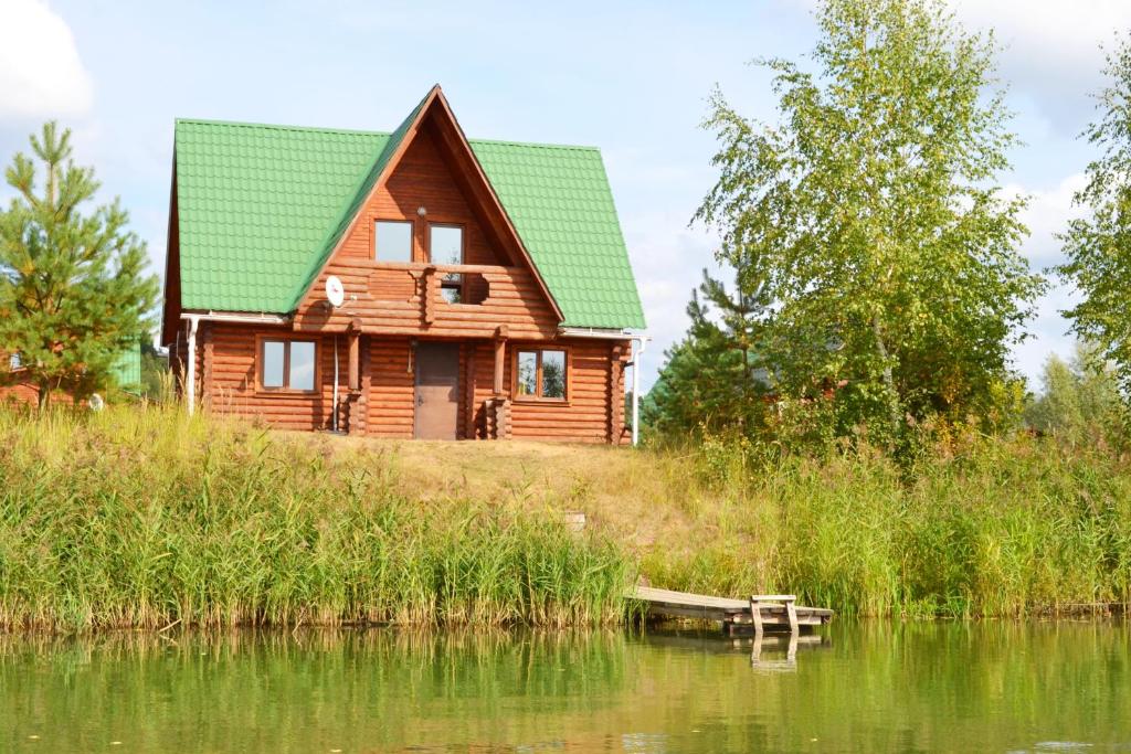 a wooden house with a green roof next to a lake at Fishing Club Litvinovo in Litvinovo