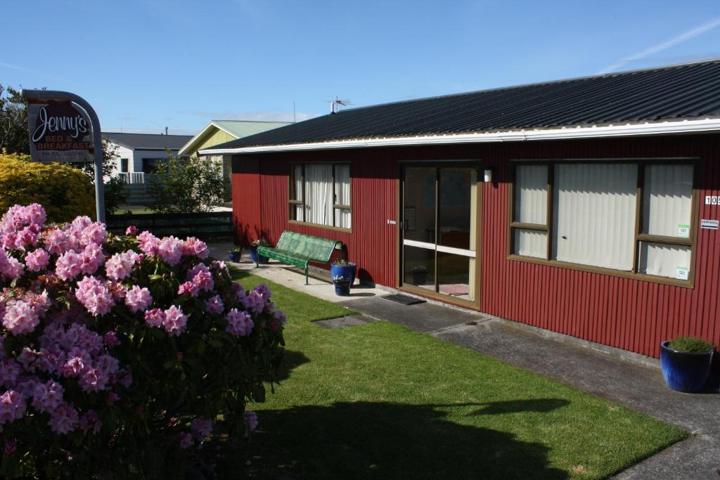 a red building with a bench in a yard with flowers at Jenny's Bed & Breakfast in New Plymouth