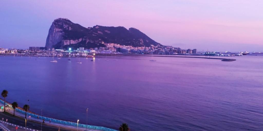 una gran masa de agua con una ciudad y una montaña en Apartamentos vista a tres continentes, en La Línea de la Concepción