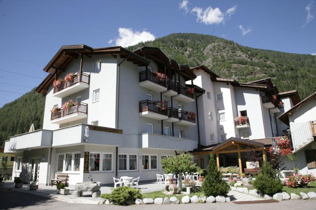 a large white building with a mountain in the background at Hotel Santoni in Ossana