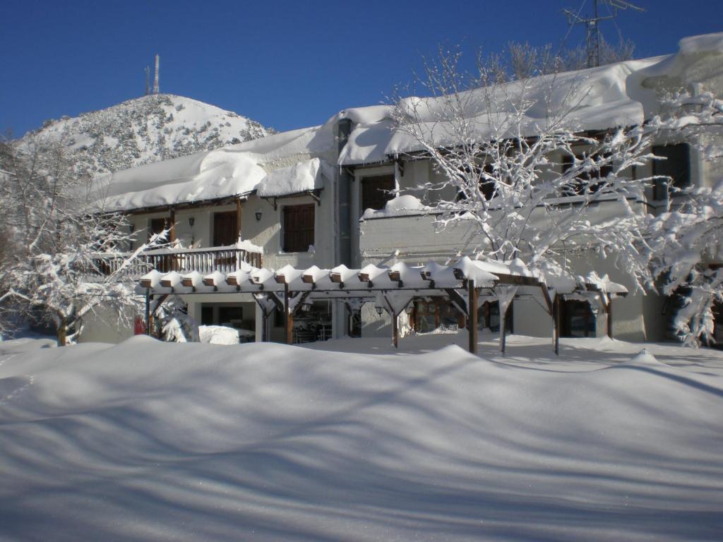 una casa ricoperta di neve con alberi in primo piano di Neos Omalos Hotel a Omalos