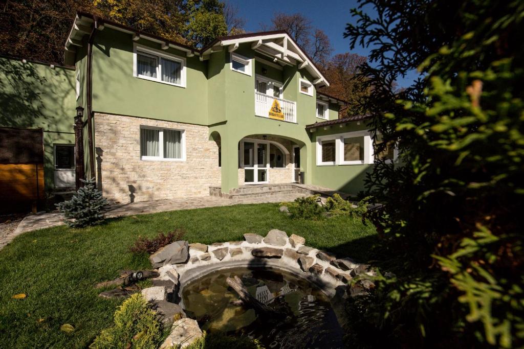 ein grünes Haus mit einem Teich davor in der Unterkunft Drachenhaus Urban Villa in Braşov