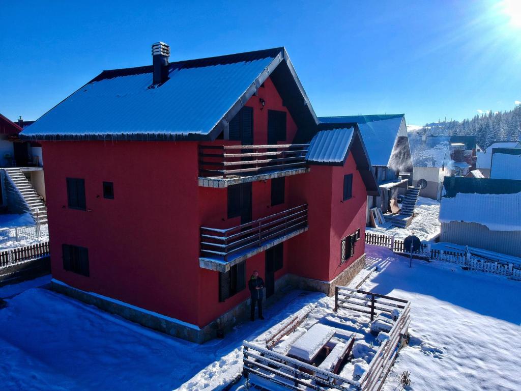 a red house in the snow with the sun behind it at Apartments Radingturs in Žabljak