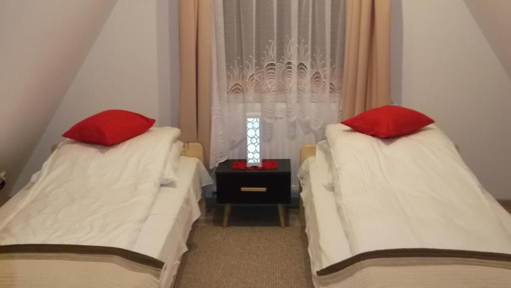 two beds with red pillows in a room with a window at Apartamenty Lejówka in Chochołów