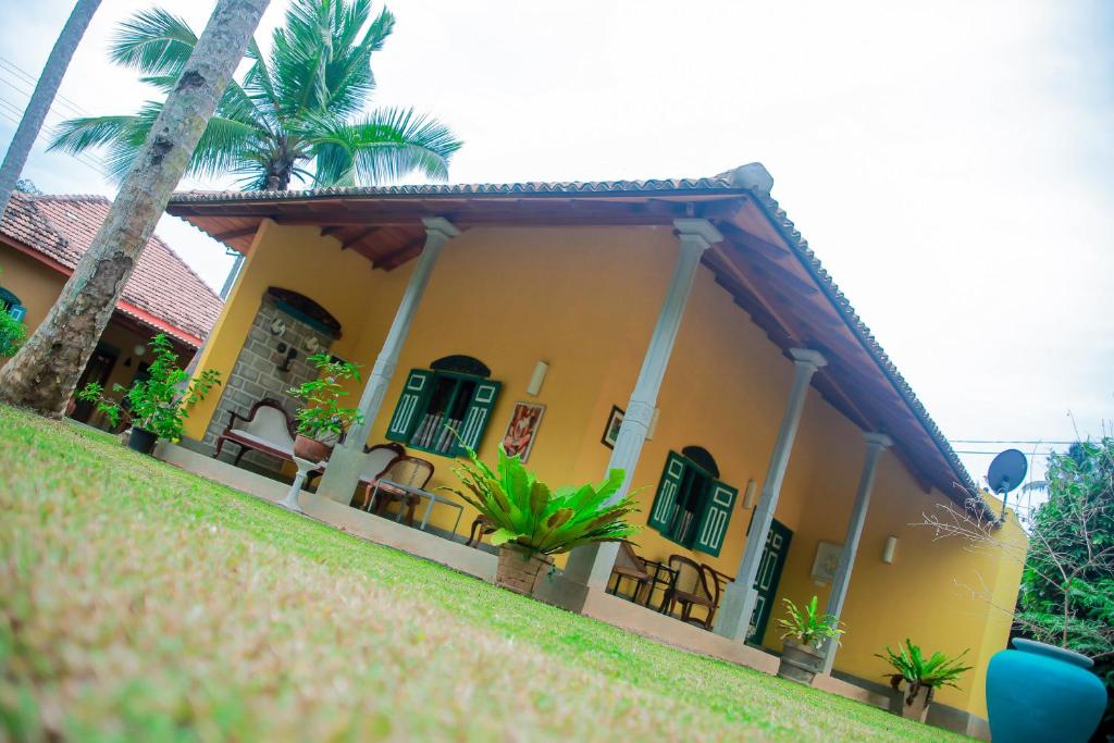 a yellow house with chairs and palm trees at Kurumba Villas in Bentota