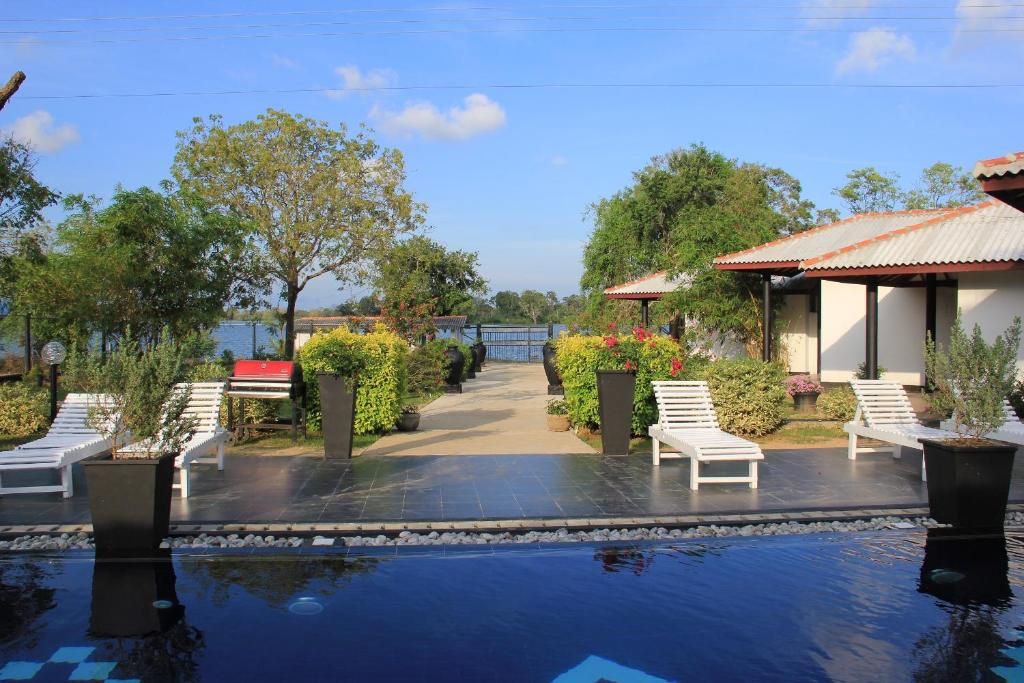 a pool with white chairs next to a building at Flower Garden Lake Resort in Tissamaharama