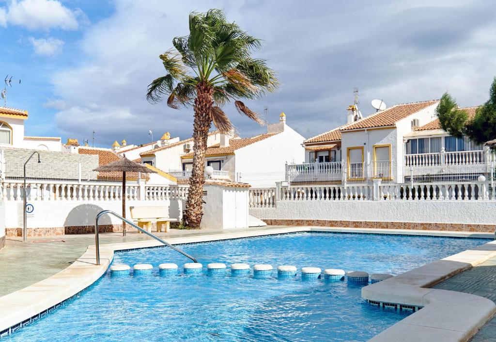 a swimming pool in front of a house with a palm tree at Apartment Eden in Guardamar del Segura