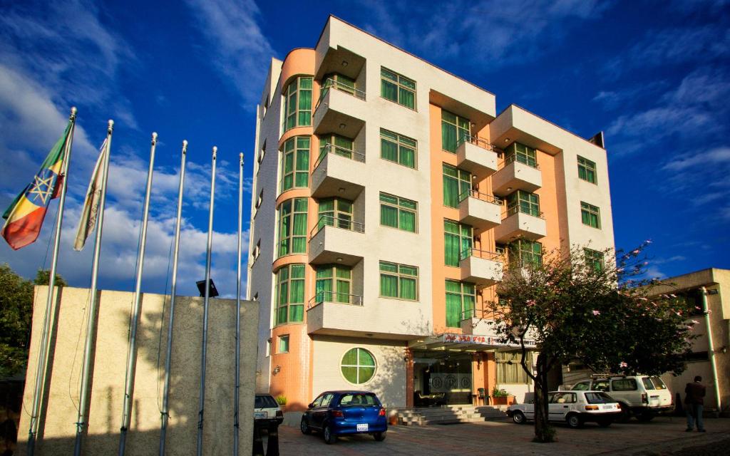 wysoki budynek z samochodami zaparkowanymi przed nim w obiekcie Hera Addis Hotel w Addis Abebie