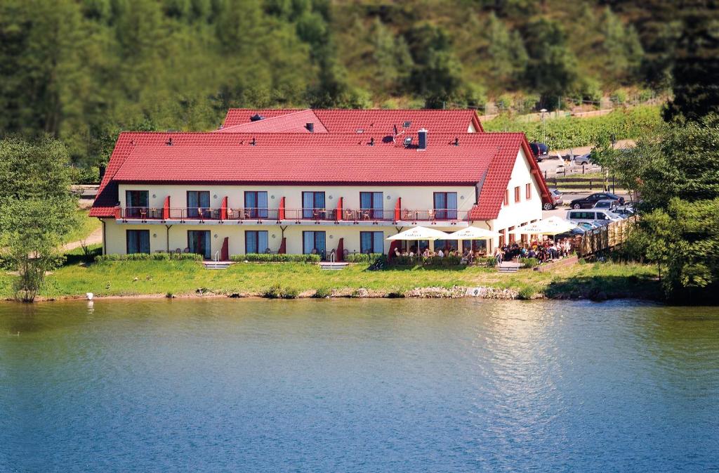 a large building with a red roof next to a lake at Seehotel Weit Meer in Waren