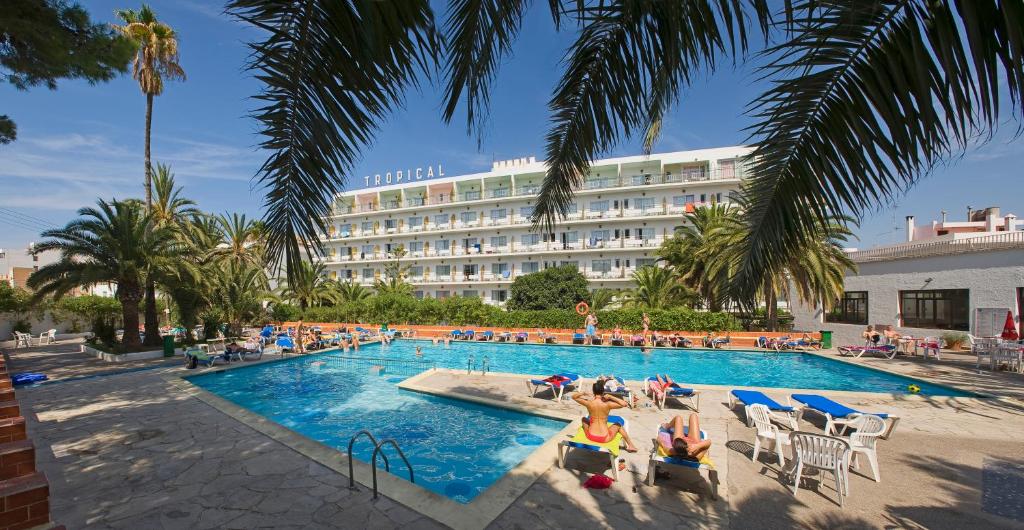 un hotel con una piscina con gente sentada en sillas en Hotel Tropical, en San Antonio