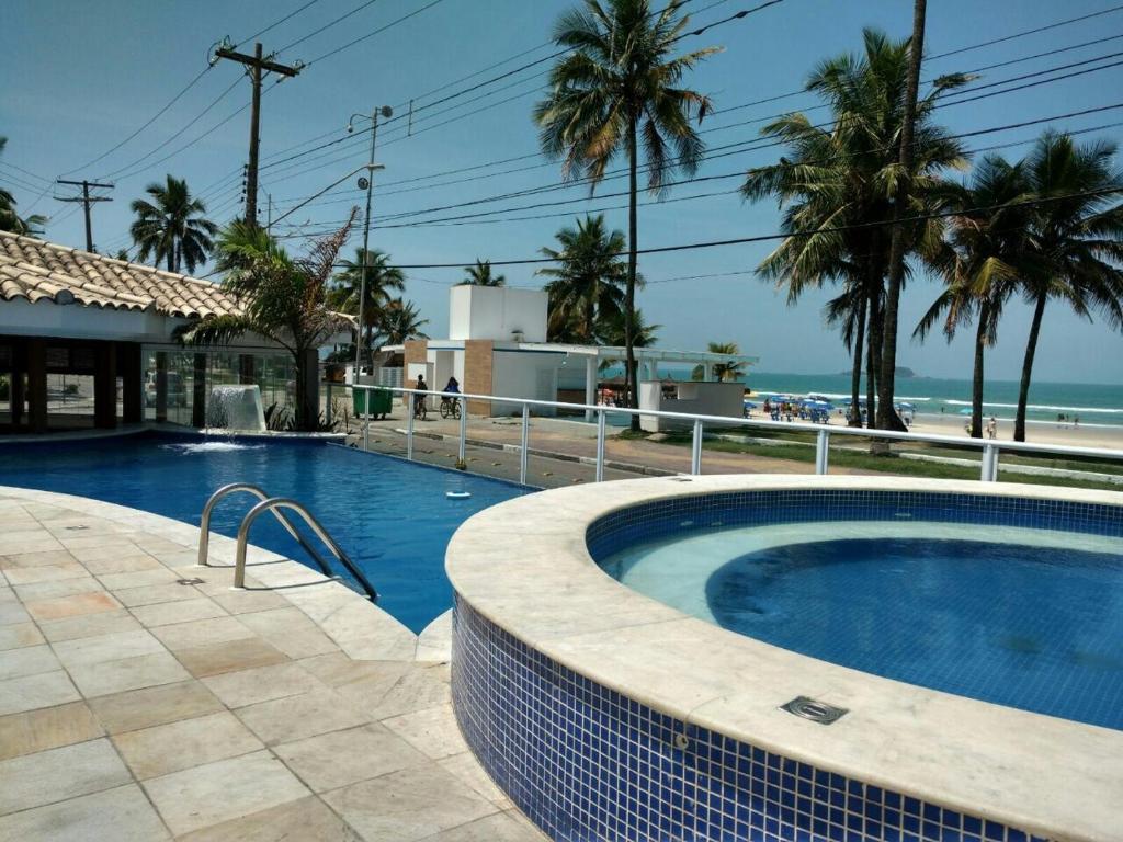 a swimming pool next to a beach with palm trees at Jequitiba Hotel Frente ao Mar in Guarujá