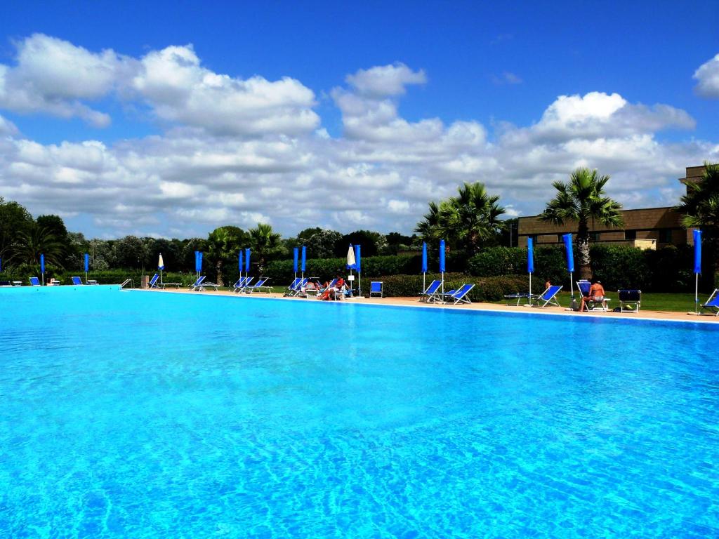 a large blue swimming pool with chairs and people at Cosmopolitan Golf & Beach Resort in Tirrenia