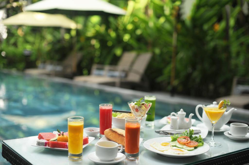 a table with breakfast food and drinks next to a pool at East West Villa in Hoi An