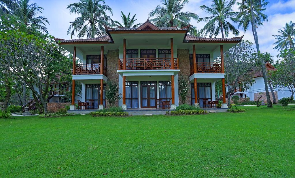 a house with a green lawn in front of it at Mangsit Suites by Holiday Resort Lombok in Mangsit
